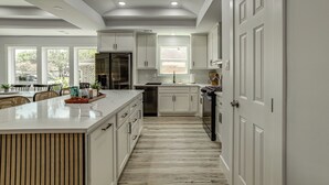 A modern kitchen with white cabinetry, a central island, and a view to the dining area. - Walk to Main St Tomball! Family Retreat w/ Yard (Tomball)