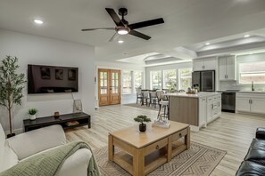 A modern kitchen with white cabinets, a stainless steel refrigerator, and a dining area with a wooden table and chairs.