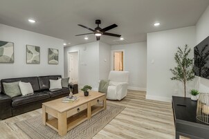 Una sala de estar moderna con un sofá de cuero negro, una mesa de centro de madera, un sillón blanco y un ventilador de techo.