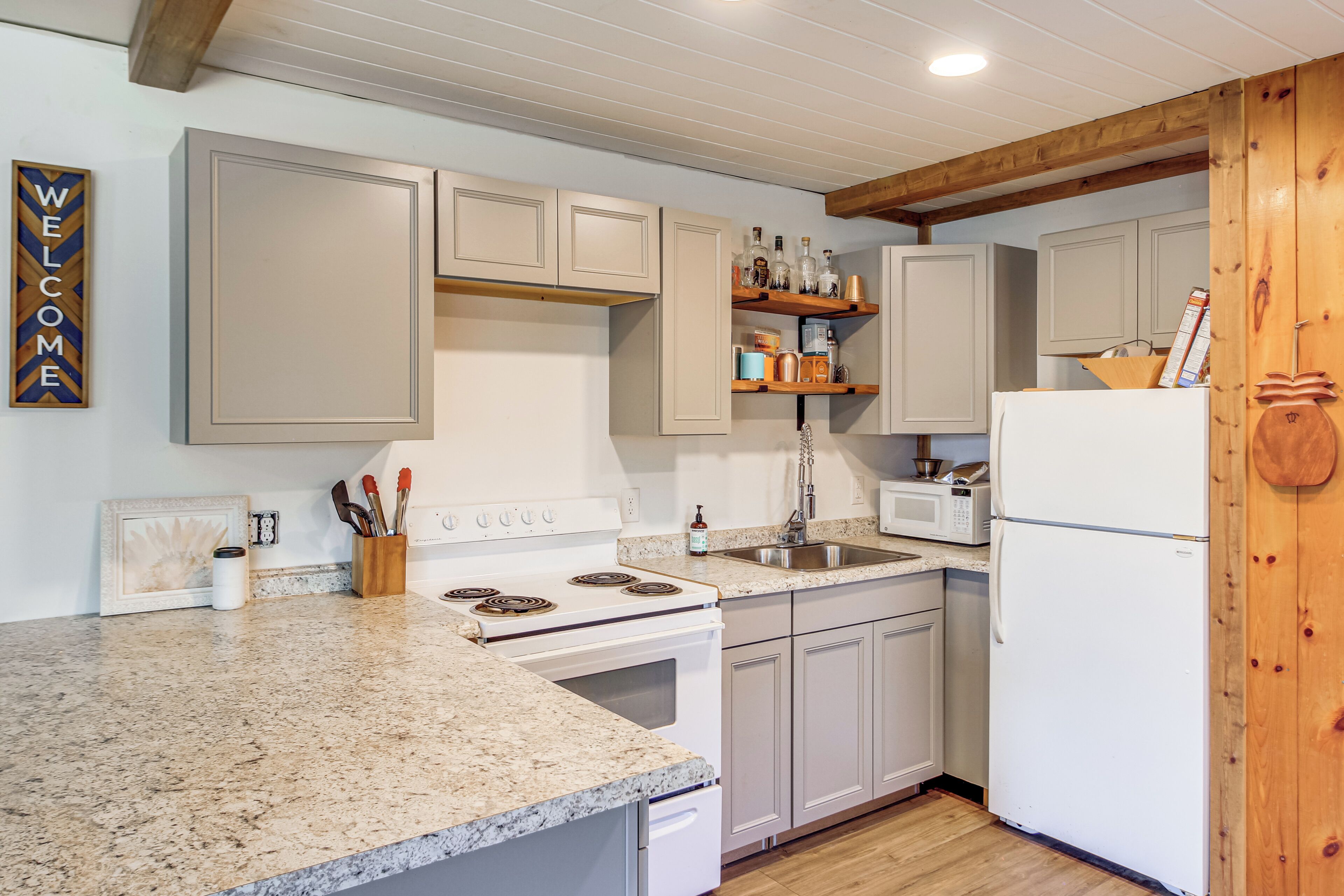 A kitchen with white cabinets, a granite countertop, a stove, a sink, and a microwave.