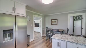 Eine Küche mit weißen Schränken, einem Edelstahlkühlschrank, einem Holzespeisetisch mit Stühlen und einer Uhr an der Wand.