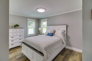 A bedroom with a bed, dresser, and a window with blinds.