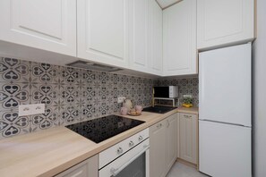 Une cuisine avec des meubles blancs, une cuisinière noire et un dosseret à motifs.