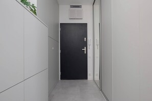 Un couloir étroit avec une porte noire, des murs blancs et une plante sur le côté gauche.