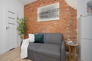Een kamer met een bakstenen muur, een grijze bank, een witte deur en een klein houten tafeltje met een tijdschrift.