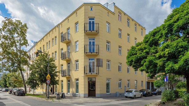 A multi-story yellow building with balconies, a pedestrian area, and parked cars. - Stylish Apartment for 4 People | Near the Theatre (Warszawa)