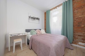 Ein Schlafzimmer mit Bett, Schreibtisch und einem fenster mit Vorhängen.