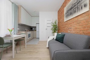 Eine moderne Küche mit weißen Schränken, einem Esstisch mit Stühlen und einem grauen Sofa in einem Wohnbereich mit Ziegelwand und einem gerahmten Bild.