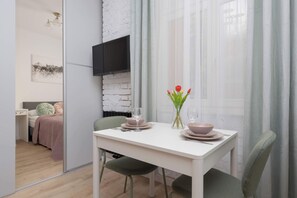 A modern dining area with a white table, green chairs, and a vase with red flowers. - Stylish Apartment for 4 People | Near the Theatre (Warszawa)