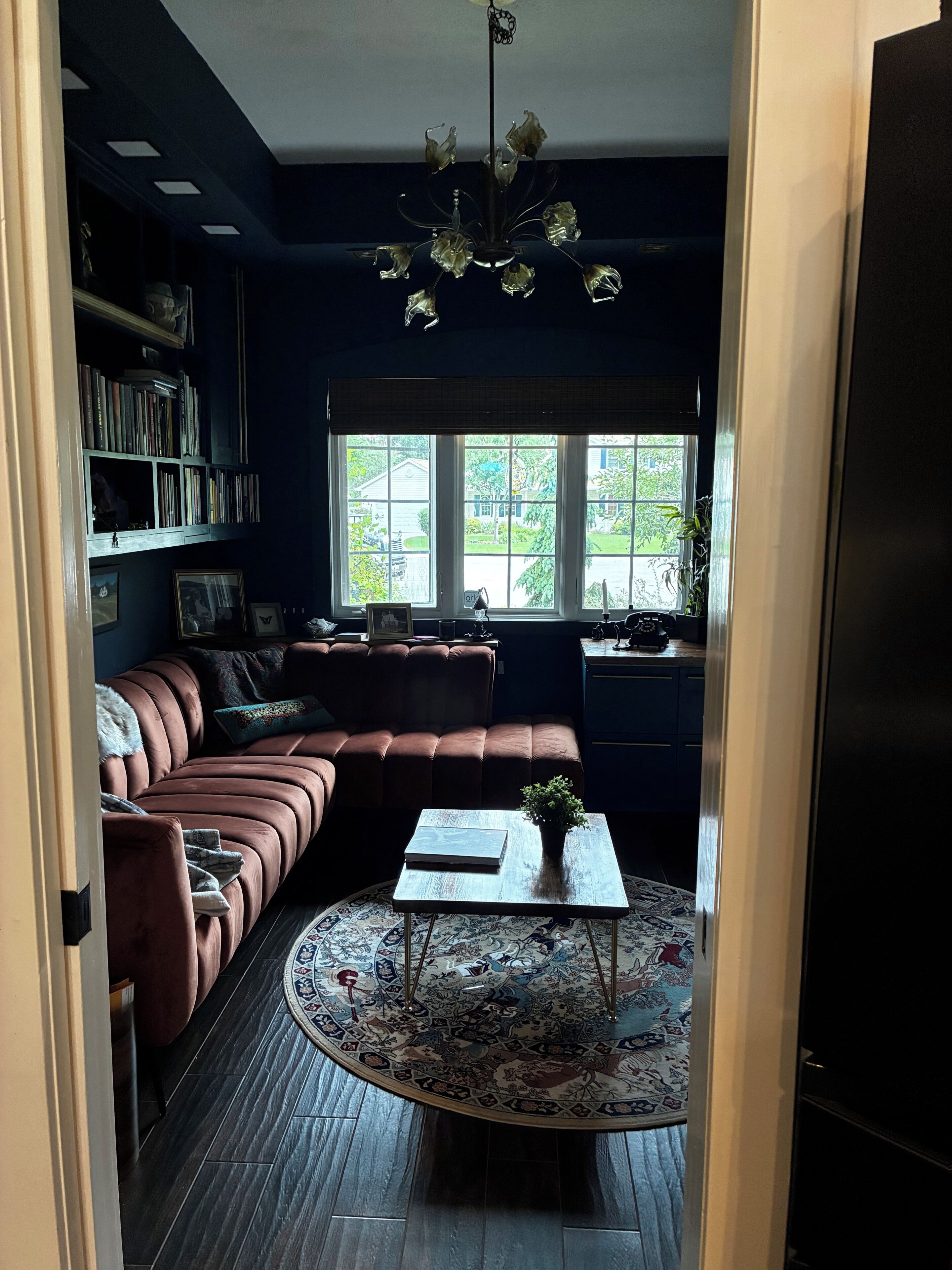 Ein Zimmer mit Ecksofa, rundem Couchtisch, Bücherregal und Fenster mit Blick auf Grünfläche.