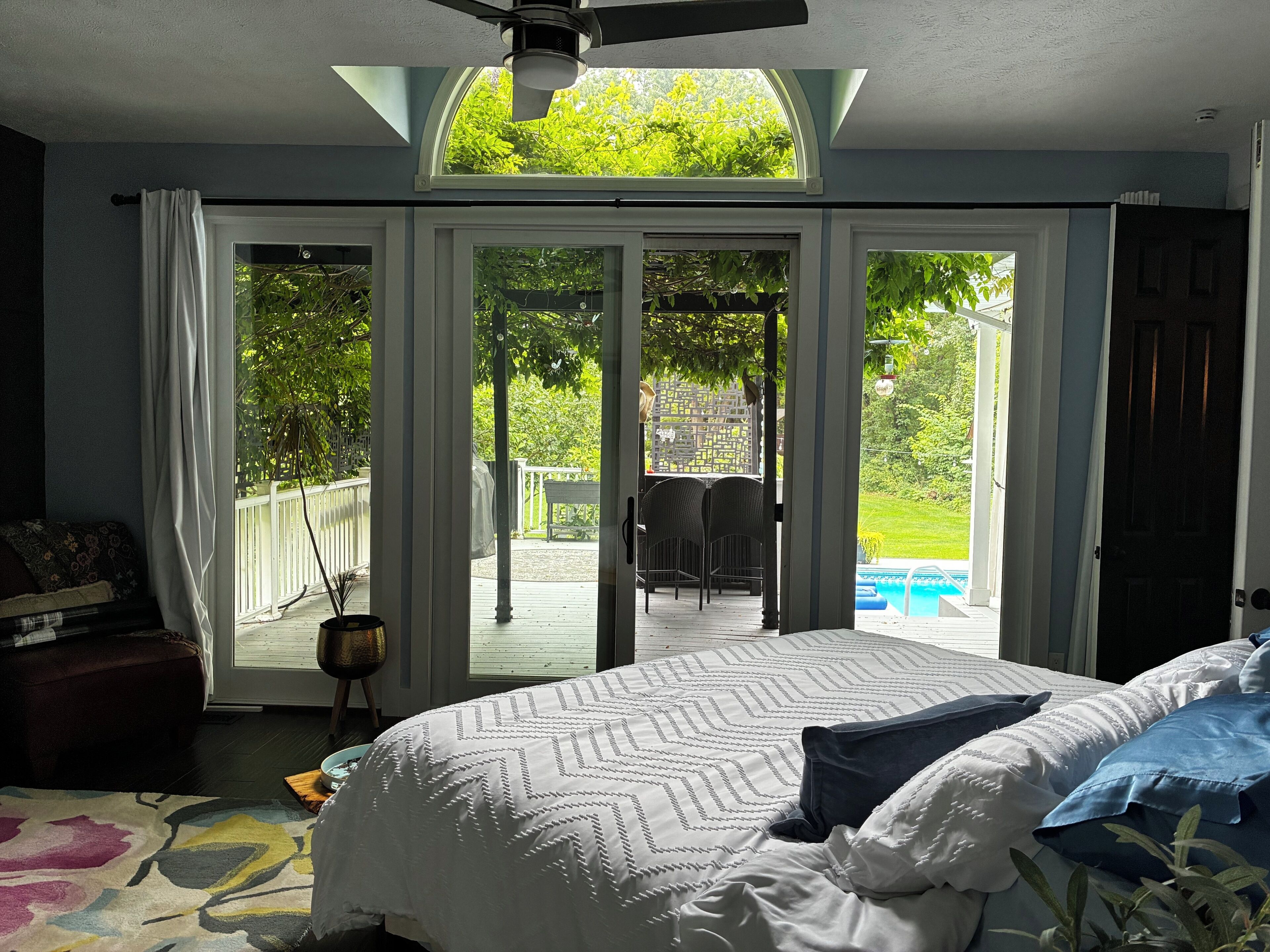 Ein Schlafzimmer mit einem Bett, einem Deckenventilator und Blick auf einen Hinterhof mit Pool.
