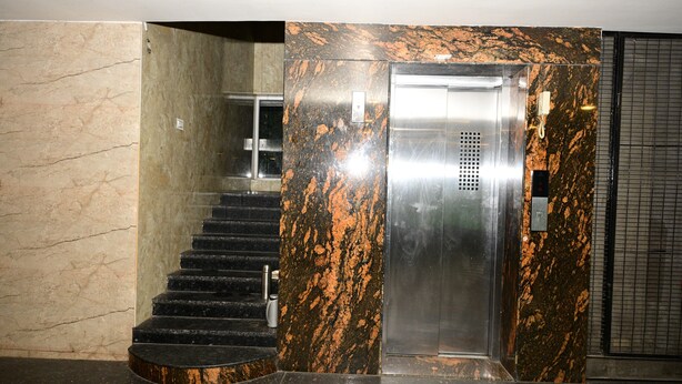 An elevator with a metallic finish, adjacent to a staircase with black steps and a marble wall with orange patterns. - HOTEL GRAND CITY (Vijayawada)