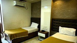 A hotel room with two single beds, a bedside table with a phone, a wall-mounted air conditioner, and a marble-patterned wall. - HOTEL GRAND CITY (Vijayawada)