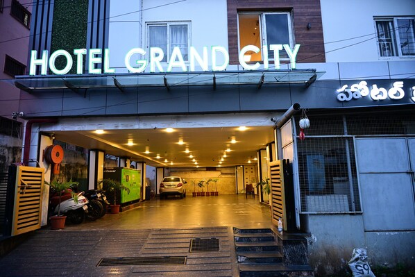 The entrance of a hotel with a neon sign, a covered parking area, and a staircase leading inside.