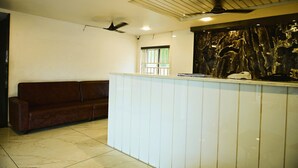 A reception area with a reception desk, a ceiling fan, a brown sofa, and a window with blinds. - HOTEL GRAND CITY (Vijayawada)