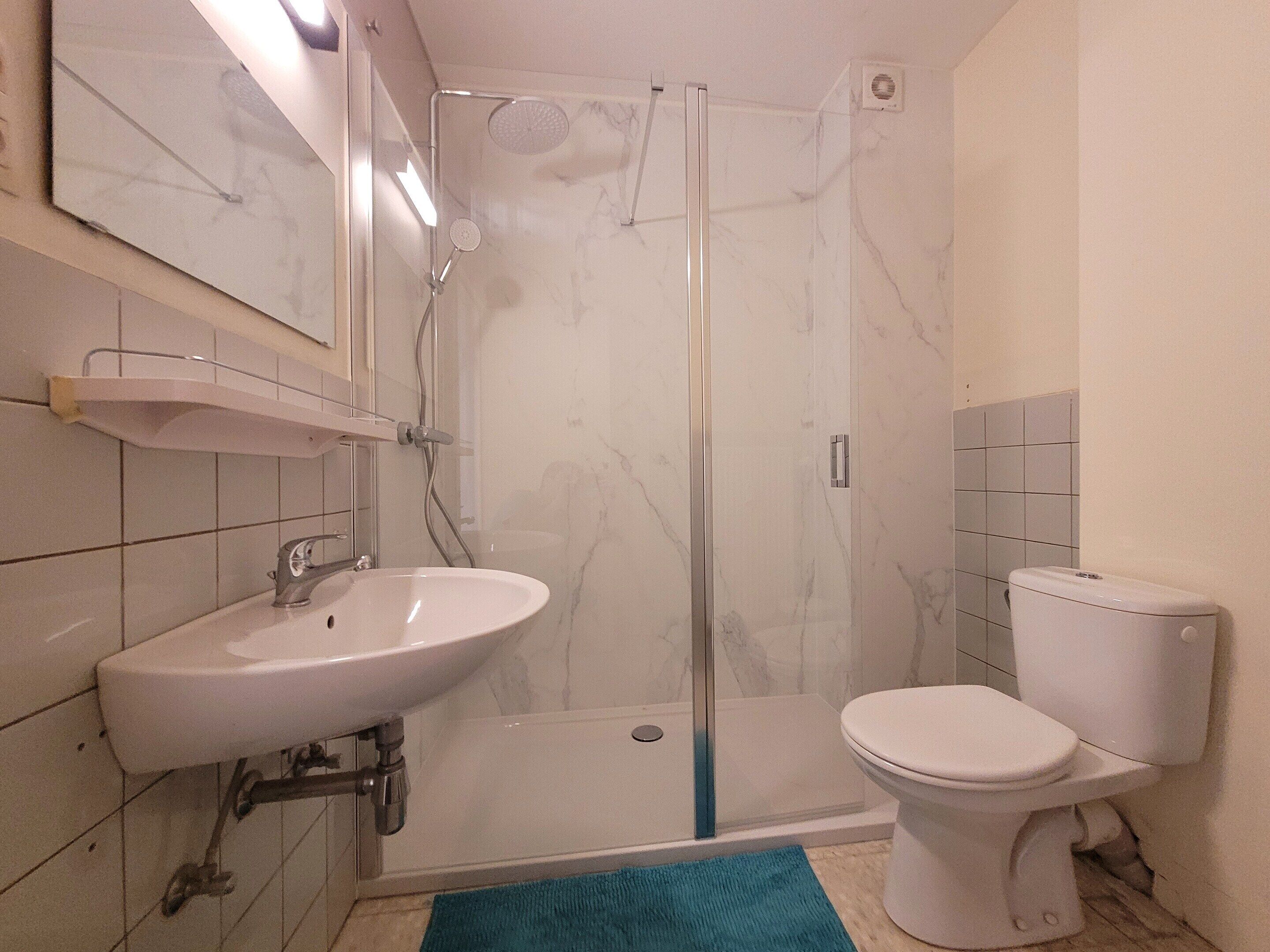 A bathroom with a glass-enclosed shower, a white sink, and a toilet.