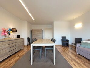 Ein modernes Wohnzimmer mit einem Holzesstisch, schwarzen Stühlen, einem grauen Sofa und einer Holzkombination mit Schubladen.