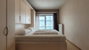 A bedroom with a bed, a wardrobe, a radiator, and a window with curtains. - Apartment on the Coast for 6 People (Middelkerke)