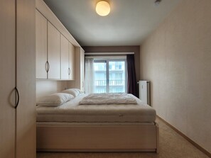 Ein Schlafzimmer mit Bett, Kleiderschrank, Heizkörper und einem fenster mit Vorhängen.