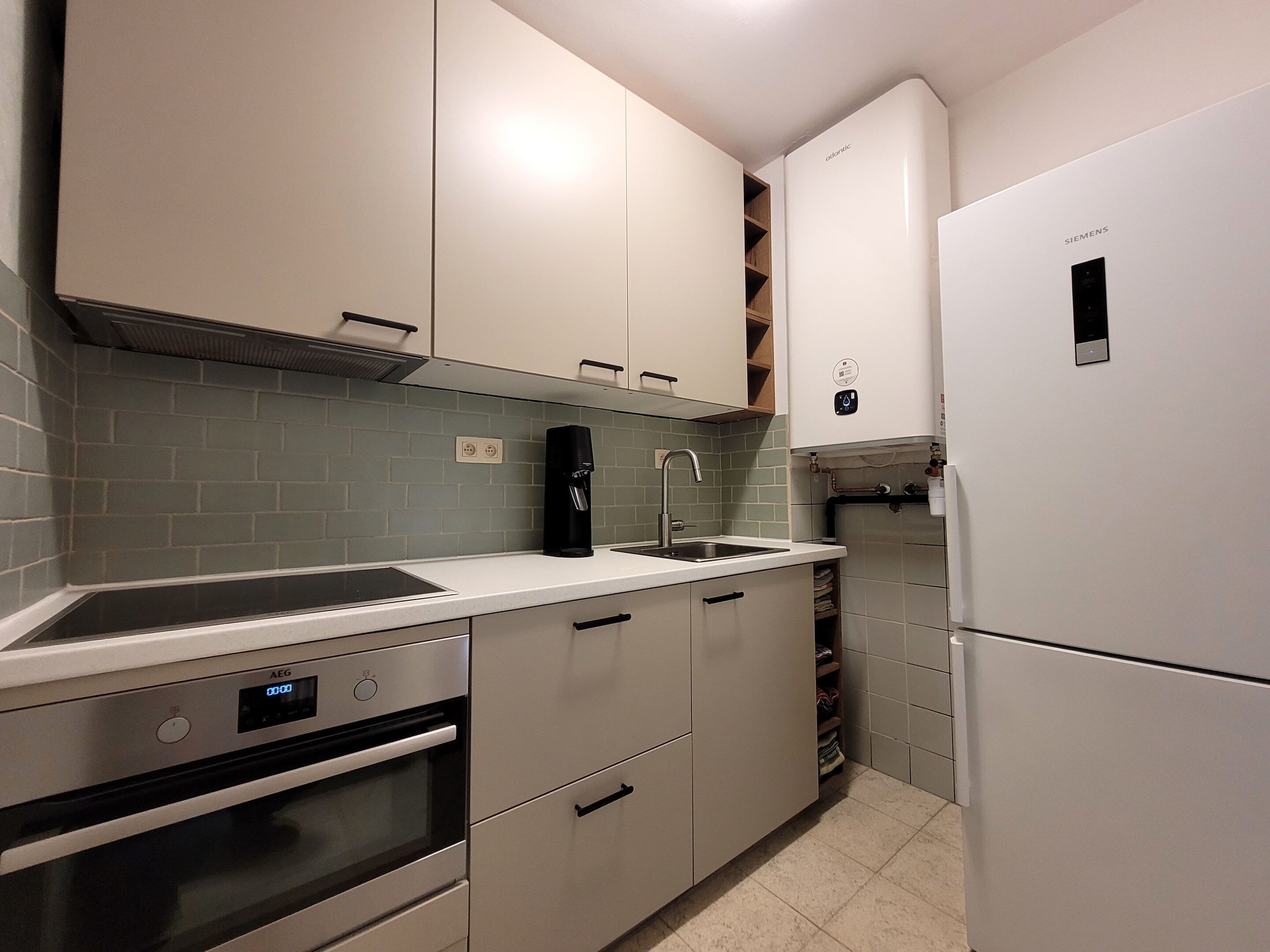 A modern kitchen with white cabinetry, a built-in oven, a coffee machine, and a Siemens refrigerator.