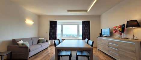 A modern living room with a sofa, dining table, chairs, a TV, and a cabinet.