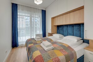 A hotel room with a large bed, a wooden headboard, a nightstand, a chair, and a window with curtains. - RentPlanet - Apartamenty Kapitanat (Gdańsk)