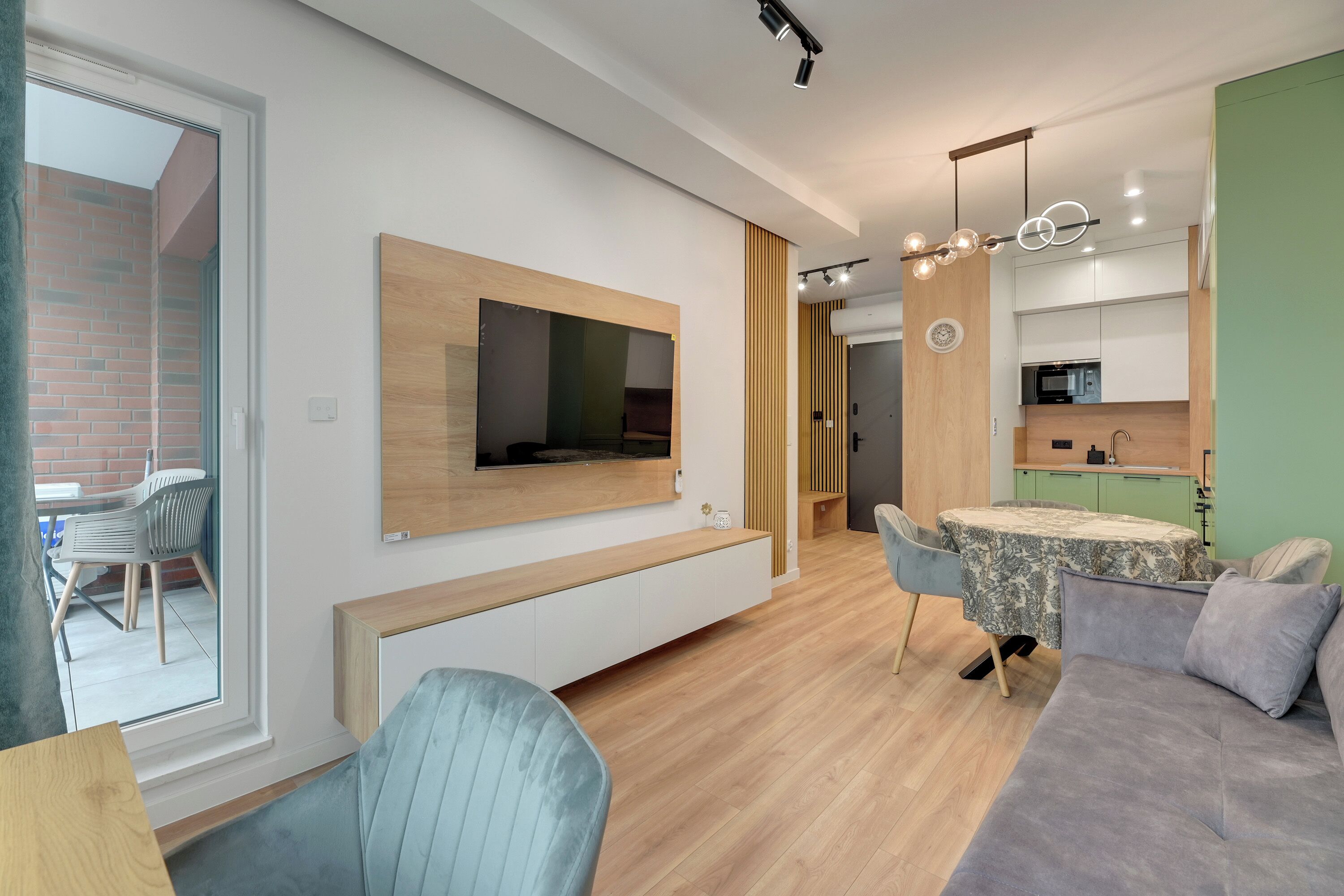 A modern living room with a flat-screen TV, a sofa, a dining table, and a kitchen area with a microwave.