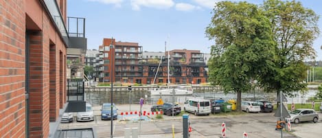 A modern building with a brick facade, a parking area with cars, and a river in the background.