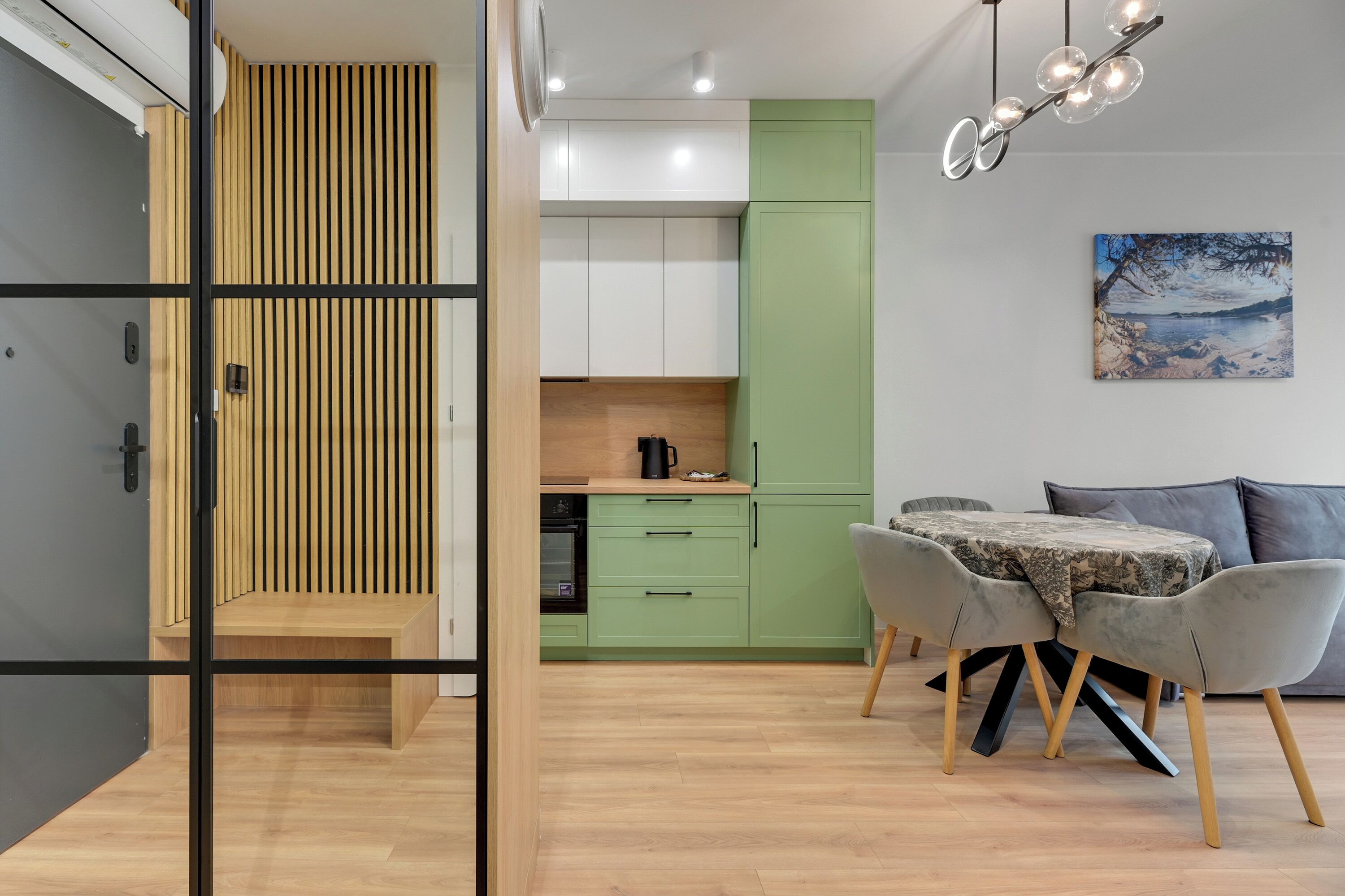 Una cocina moderna con armarios verdes, un comedor con mesa y sillas, y un cuadro en la pared.