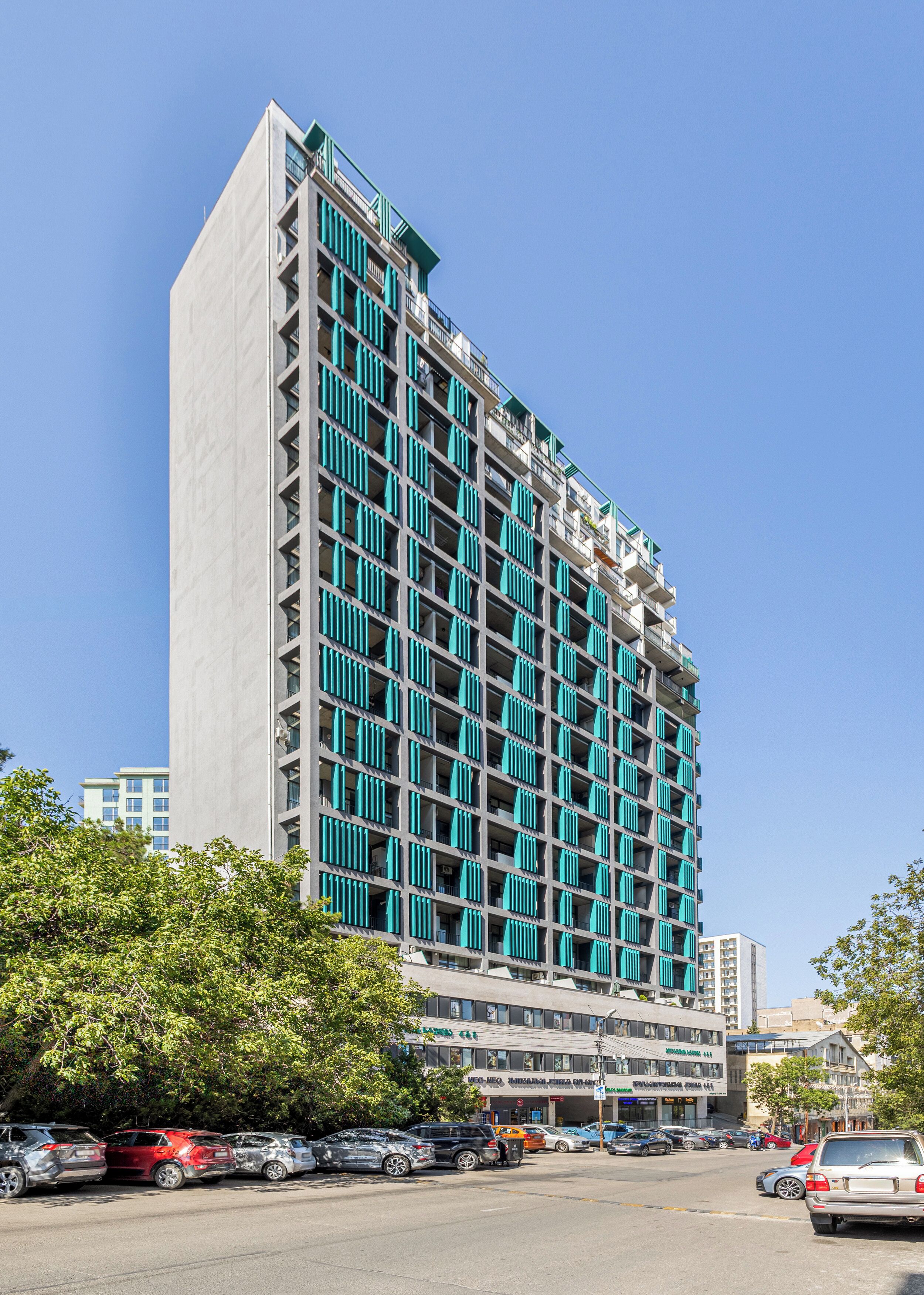 A multi-story hotel with a modern design, featuring balconies and a parking lot in front.