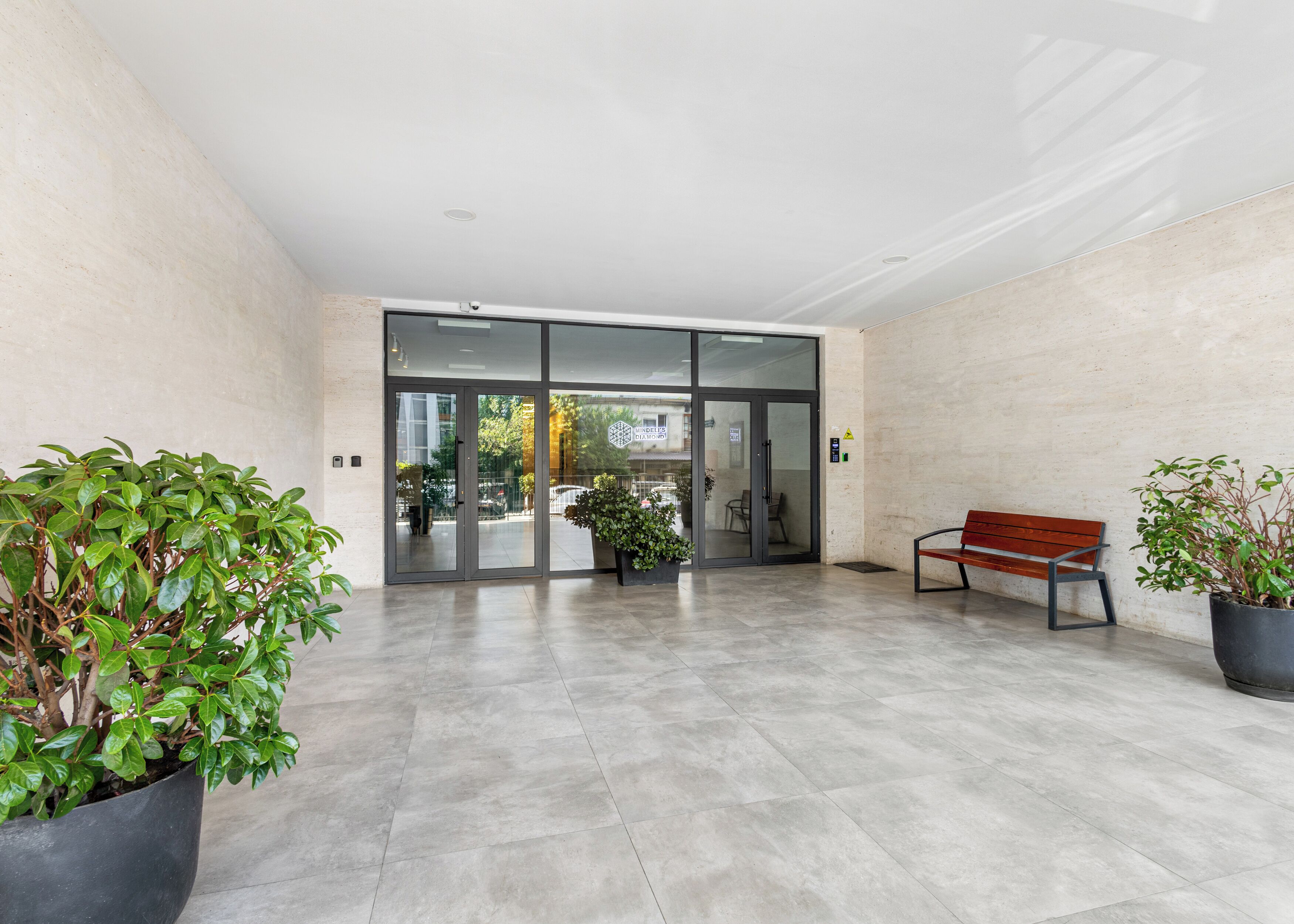 A modern lobby with a bench, potted plants, and a glass door entrance.