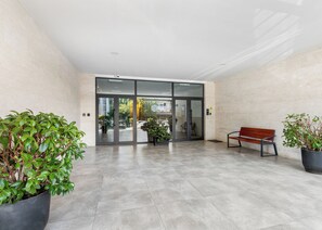 Un lobby moderno con un banco, plantas en macetas y una entrada con puerta de vidrio.