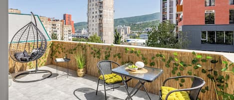 A rooftop terrace with a hanging chair, two chairs, a table, and a potted plant.