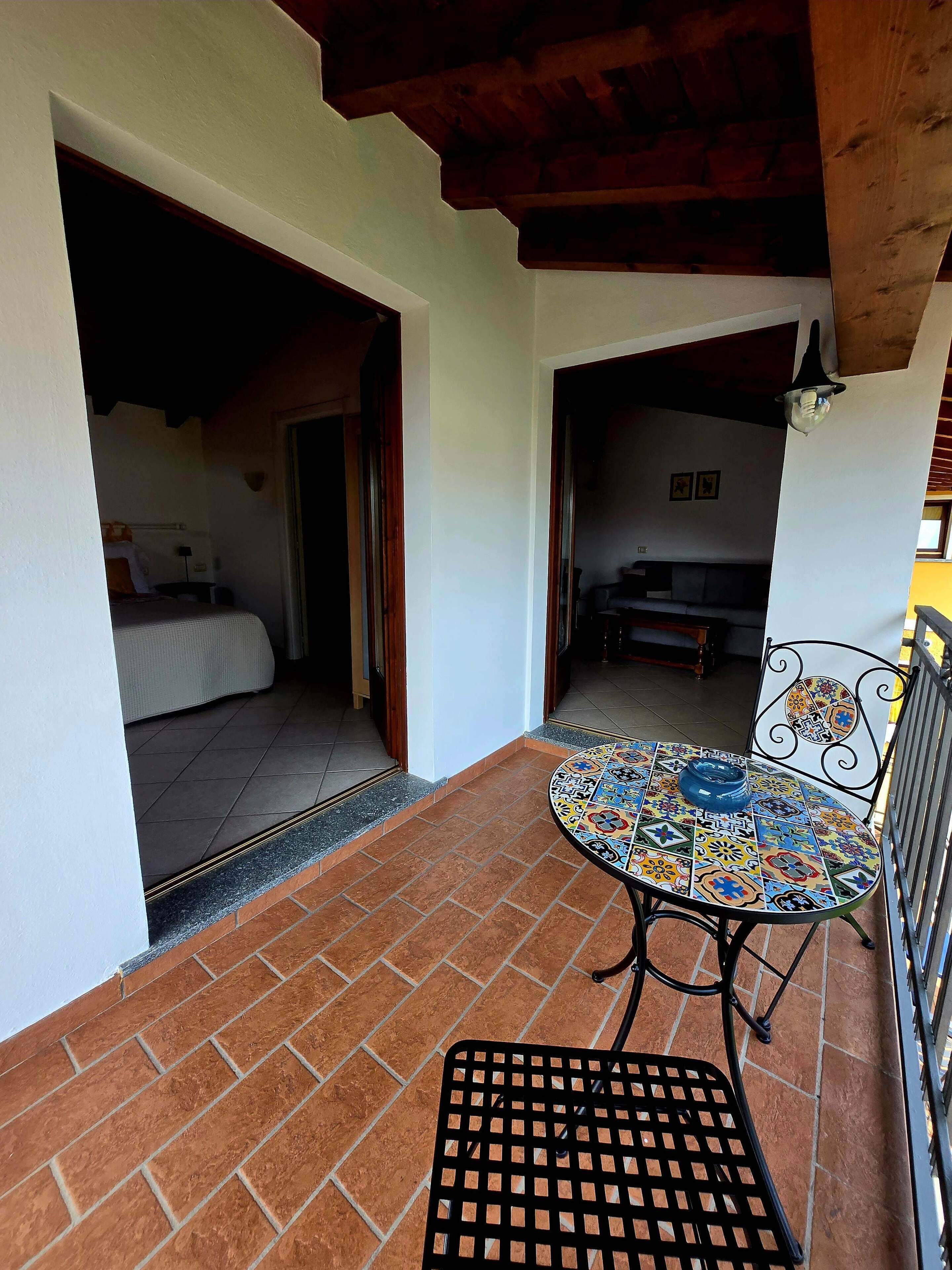 Una habitación con piso de baldosas, una cama, una mesa con mantel colorido y una silla.