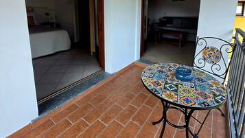 Una habitación con piso de baldosas, una cama, una mesa con mantel colorido y una silla.