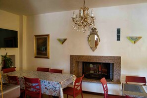 Un comedor con candelabro, chimenea y televisor montado en la pared.
