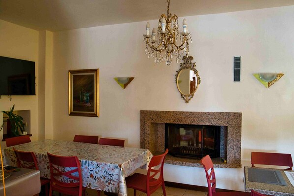 Une salle à manger agrémentée d’un lustre, d’une cheminée et d’un téléviseur fixé au mur.