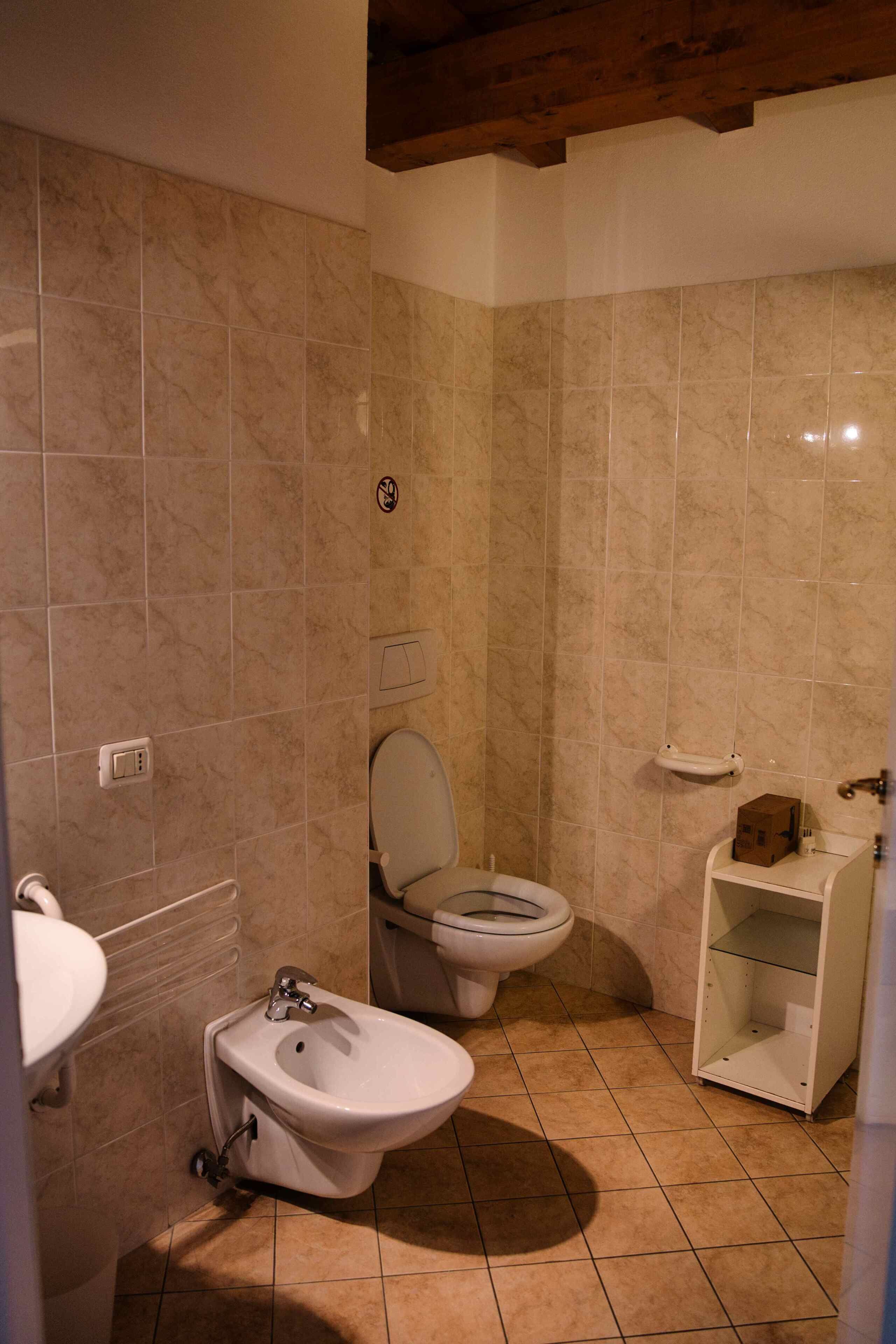 Un baño con inodoro, bidé y un estante pequeño con una caja.