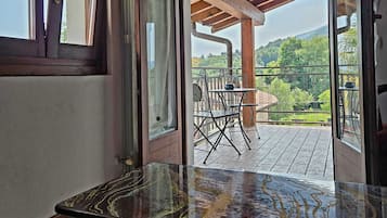 Habitación con techo de madera, una mesa de vidrio y vista a una terraza exterior con sillas y una mesa.