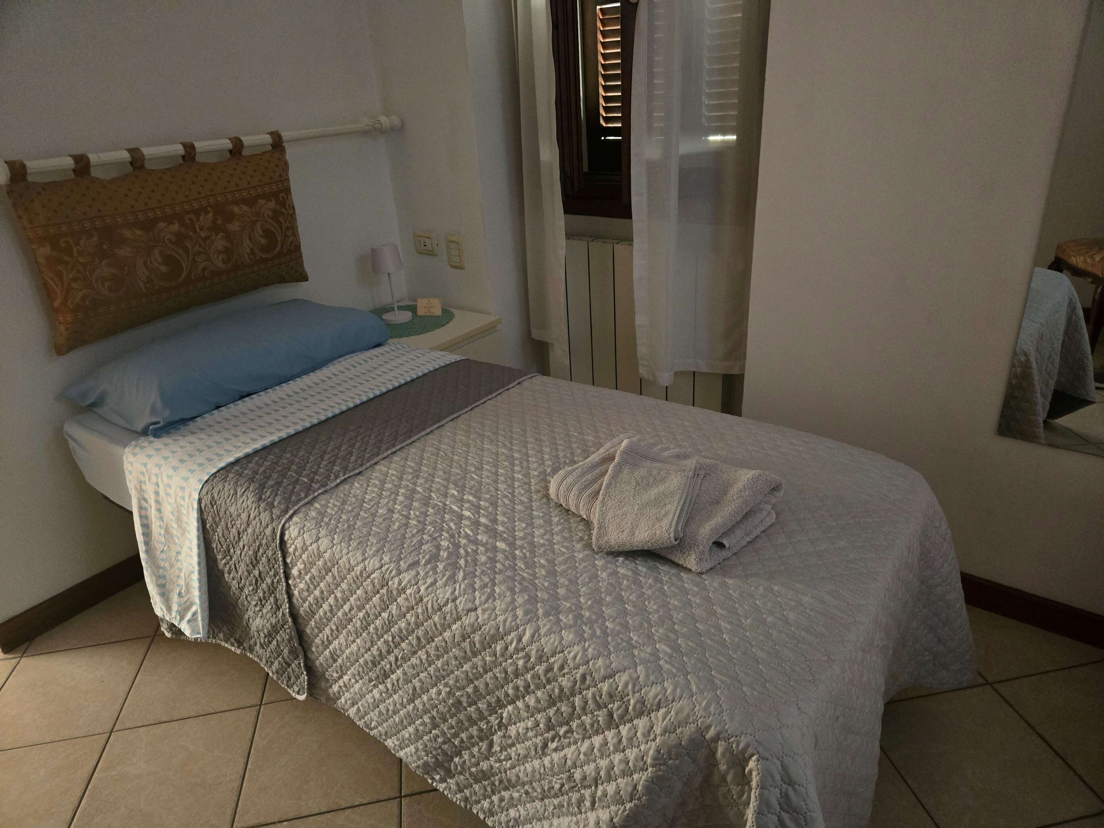 Una habitación de hotel con una cama, una mesita de noche, una lámpara y una ventana con persianas.