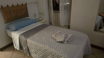 Una habitación de hotel con una cama, una mesita de noche, una lámpara y una ventana con persianas.