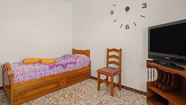 A bedroom with a bed, a chair, a television, and a wall clock. - El Rincón de Conil Apartment with Sea Views and Shared Terrace (Conil de la Frontera)