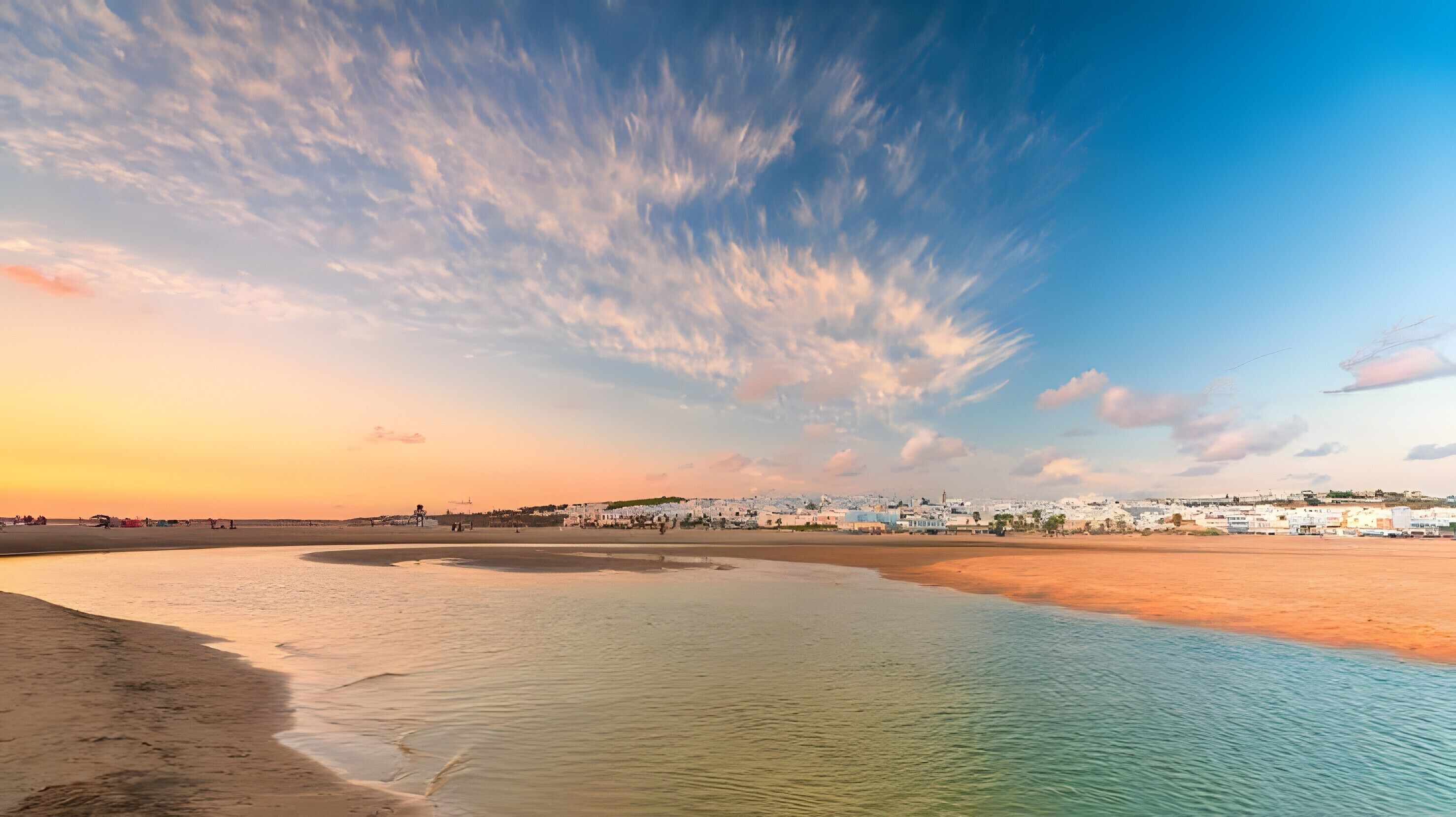 A coastal landscape with a beach, calm waters, and a town in the background.