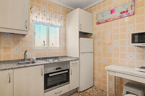 Eine kleine Küche mit Gasherd, Backofen, Kühlschrank und Mikrowelle auf einem Tisch.