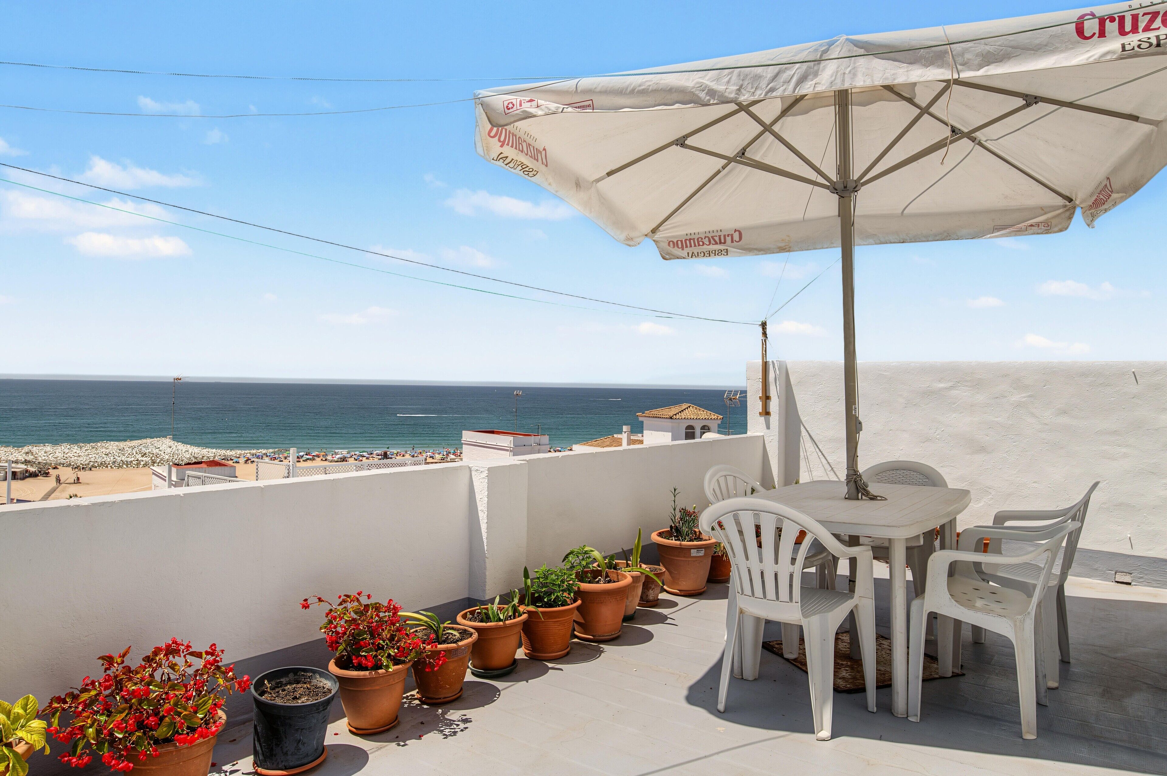 A terrace with a table and chairs, potted plants, and a view of the sea.