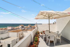 Eine Dachterrasse mit Tisch und Stühlen, Blumentöpfen und Meerblick.