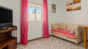 A room with a television on a wooden stand, a sofa with a striped blanket, a window with curtains, and wall art. - El Rincón de Conil Apartment with Sea Views and Shared Terrace (Conil de la Frontera)