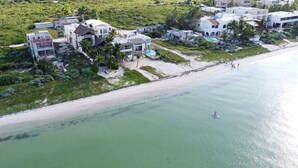 An aerial view of a coastal property with multiple buildings, a beach, and a person paddleboarding. - Villa Kakashki | Beachfront, Pool, and Padel (Yucatán)