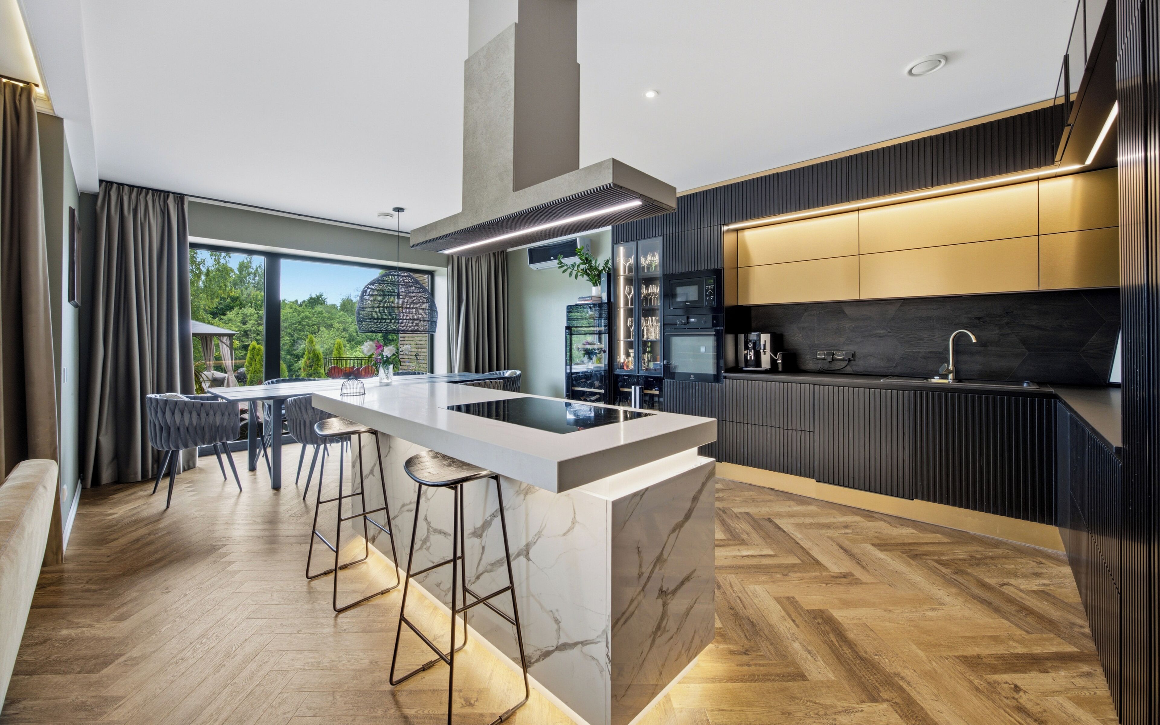 A modern kitchen with a central island, bar stools, and a dining area with a view.