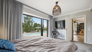 Een slaapkamer met een groot bed, uitzicht op een zwembad en een aan de muur bevestigde televisie.